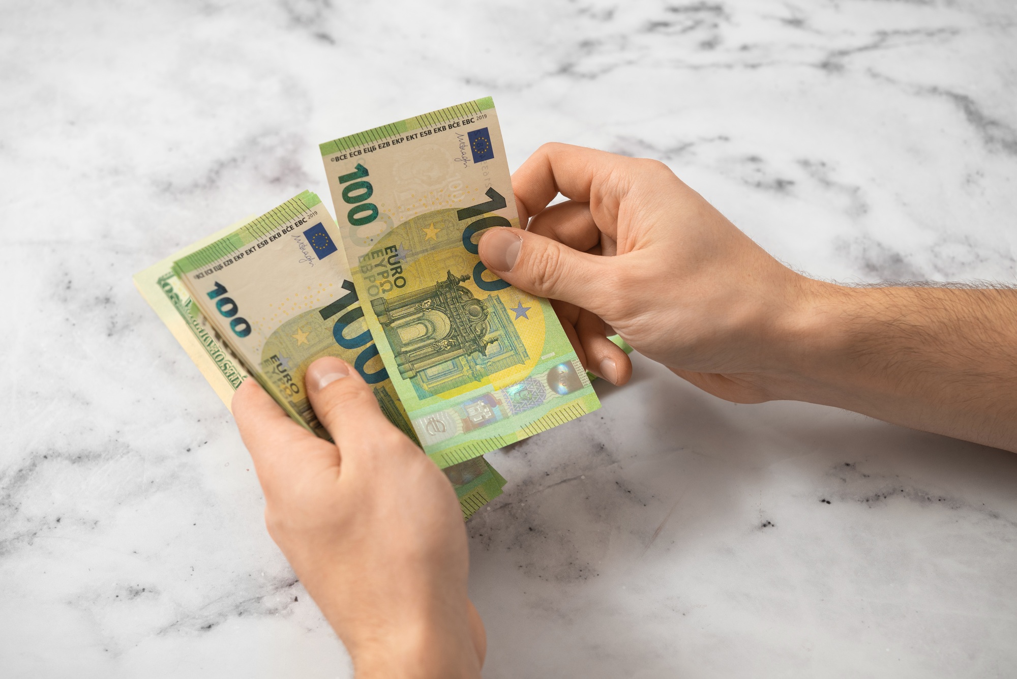 A man counts euro money with his hands on a light background